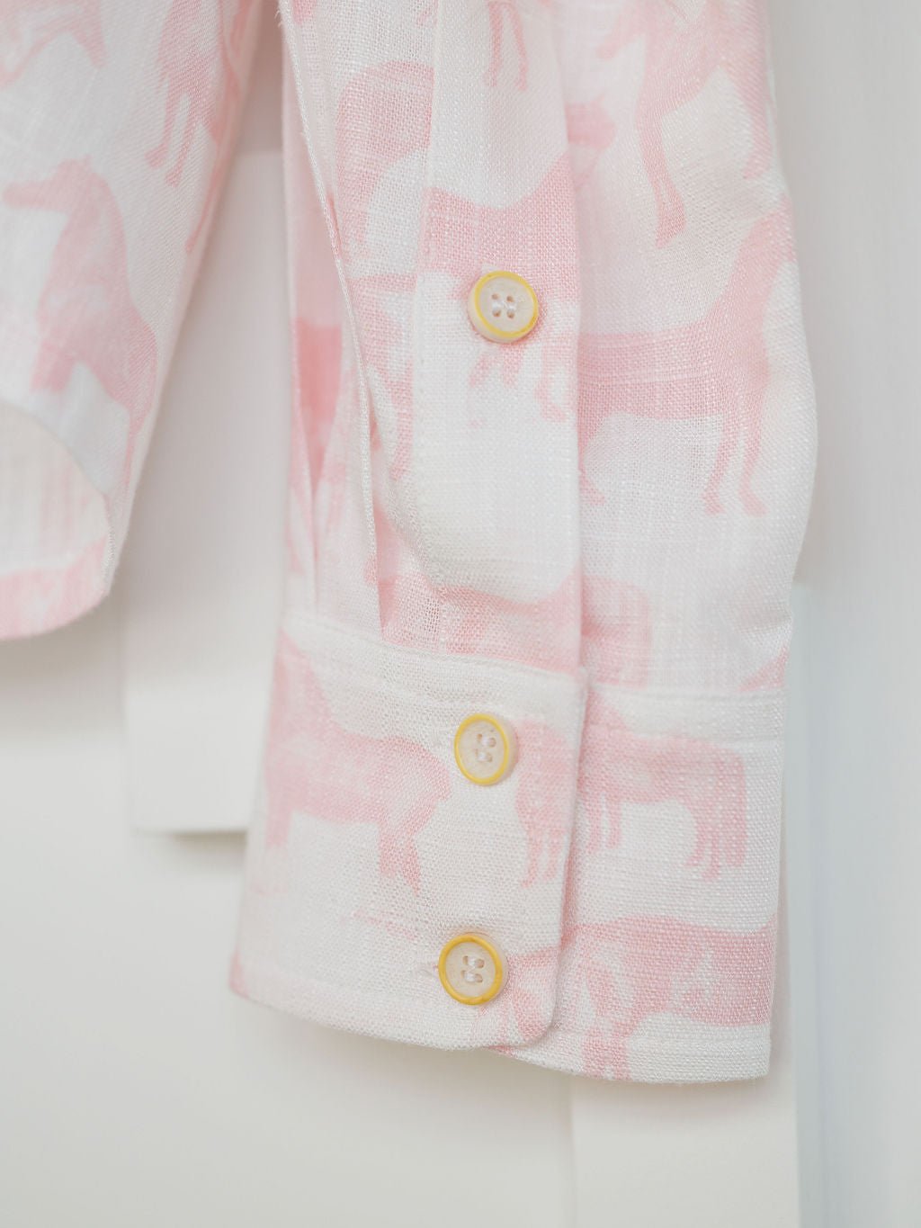 Close-up of the Savannah Sevens western life{&}style Westview Horse Graphic Button Up Top with long sleeves, three light yellow buttons, and lightweight white fabric featuring a pink horse print.