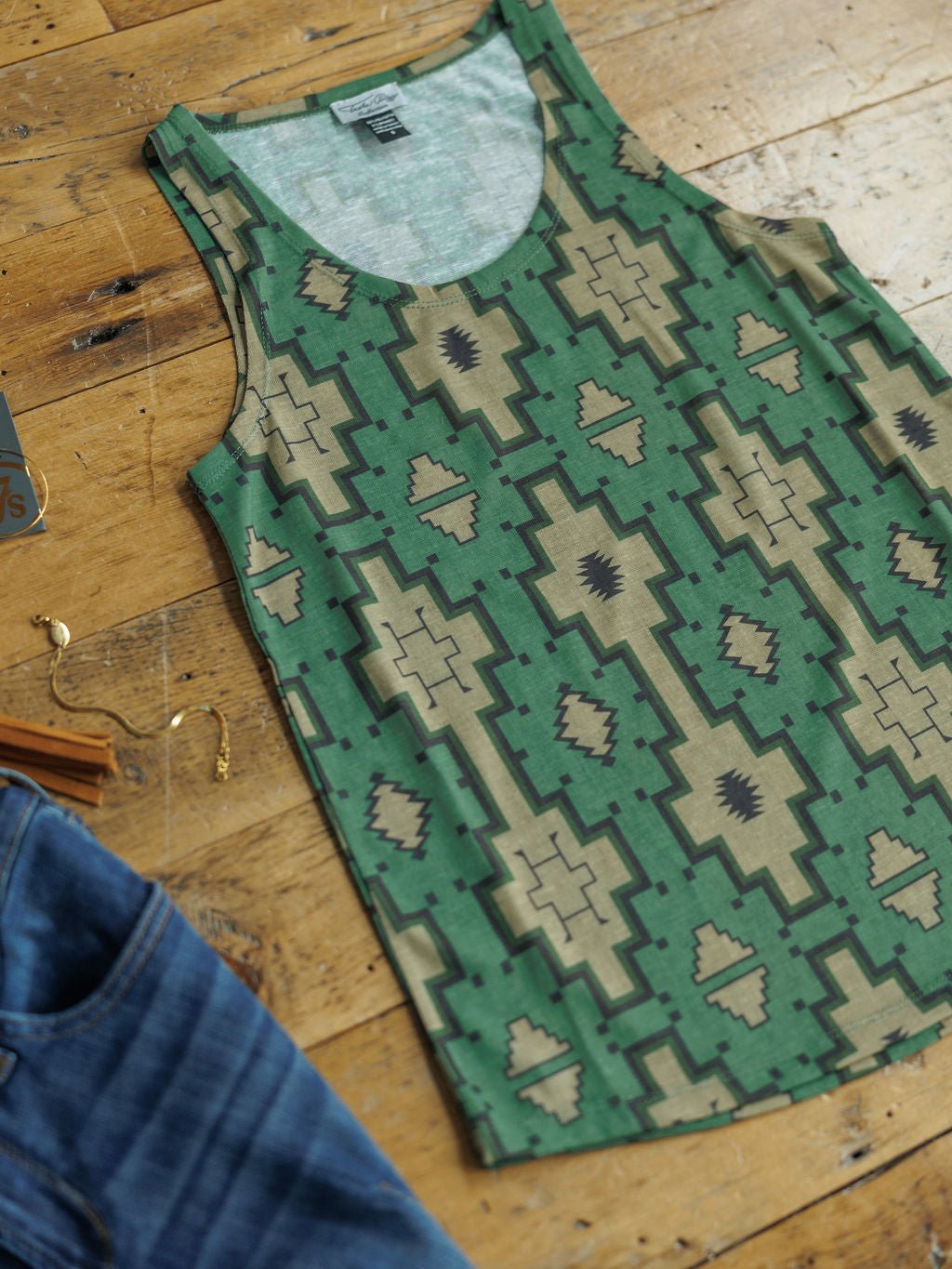 The Wetonka Southwest Tank by Savannah Sevens western life{&}style, featuring a beige and dark green geometric print, is displayed flat beside blue jeans and gold jewelry—an ideal young contemporary sizing option.