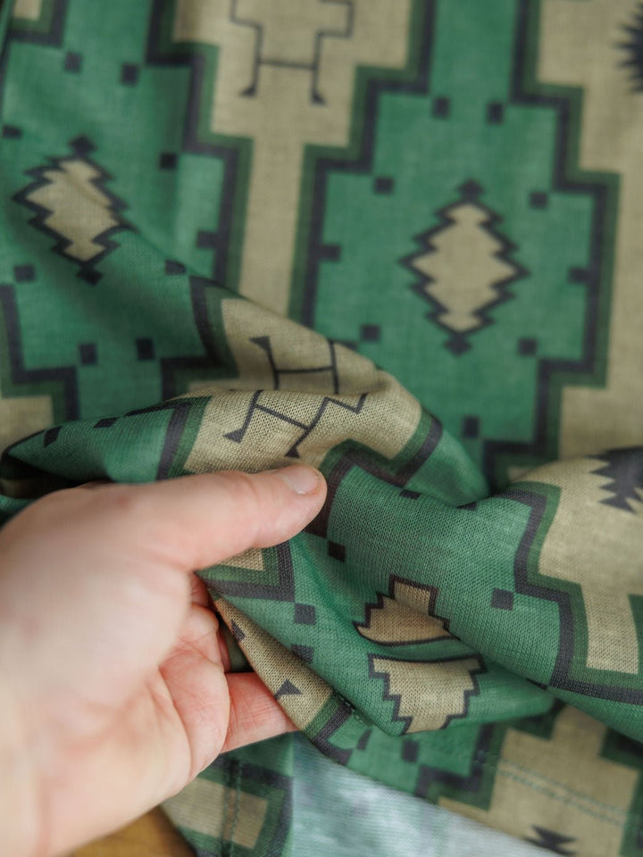 A hand holds the Wetonka Southwest Tank by Savannah Sevens western life{&}style, featuring a green, beige, and black geometric pattern with symmetrical designs inspired by Southwest prints in young contemporary sizing.