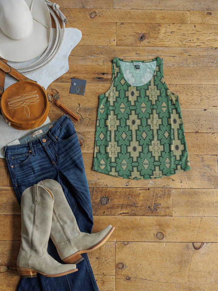 A flat lay on a wooden floor featuring the Savannah Sevens western life{&}style Wetonka Southwest Tank in green and beige, blue jeans, light gray cowboy boots, a tan round bag, and a white hat.