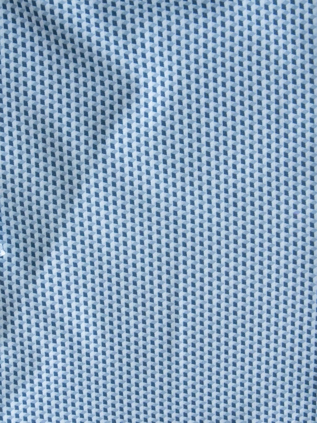 Close-up of the Willsboro Wrangler Men's Blue Button Up by Savannah Sevens western life{&}style, showcasing light blue fabric detailed with a repeating pattern of tiny dark blue squares. The geometric design and slightly wrinkled texture give this shirt its distinctive, modern look.