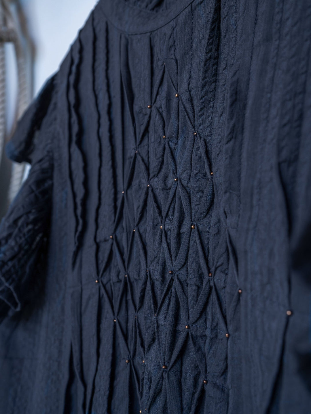 Close-up of The Winnett by Savannah Sevens western life{&}style, a midnight navy short sleeve top with intricate geometric smocking and small decorative beads creating a diamond pattern on the front.