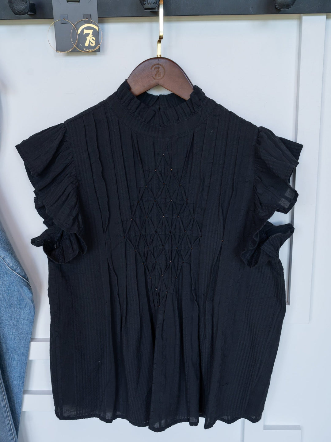 The Winnett by Savannah Sevens western life{&}style is a midnight navy short sleeve top with ruffled sleeves, a high neck, and a diamond-textured front, shown on a wooden hanger against a white background.