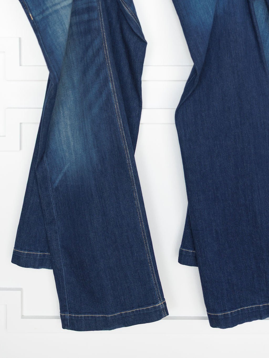 Two pairs of Ariat The Yates High Rise Wide Leg Jeans in a medium dark wash hang side by side against a white textured background.