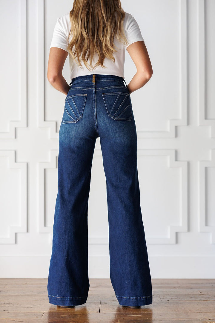 A person wearing Yates High Rise Wide Leg Jean by Ariat in a medium dark wash, featuring decorative stitching on the back pockets.