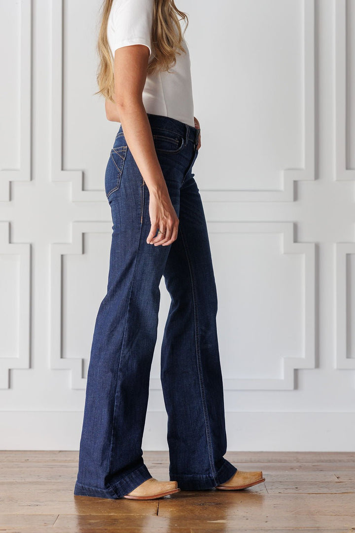Side profile of a person wearing medium dark-wash Yoakum Perfect Rise Trouser Jean *Exclusive* denim trousers and tan leather boots.