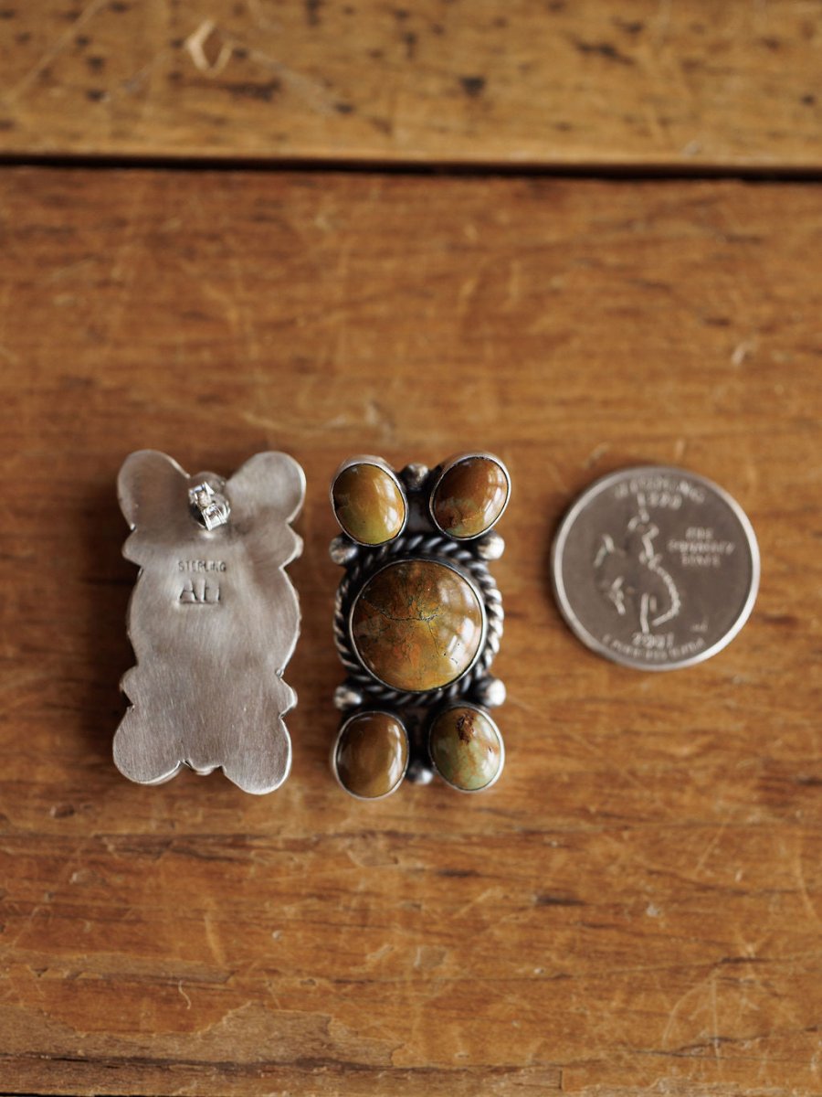The Yuma Earrings by Savannah Sevens western life{&}style, handcrafted in sterling silver with greenish-brown Nevada turquoise, are shown next to a U.S. quarter on wood, displaying both front and back for size and detail comparison.