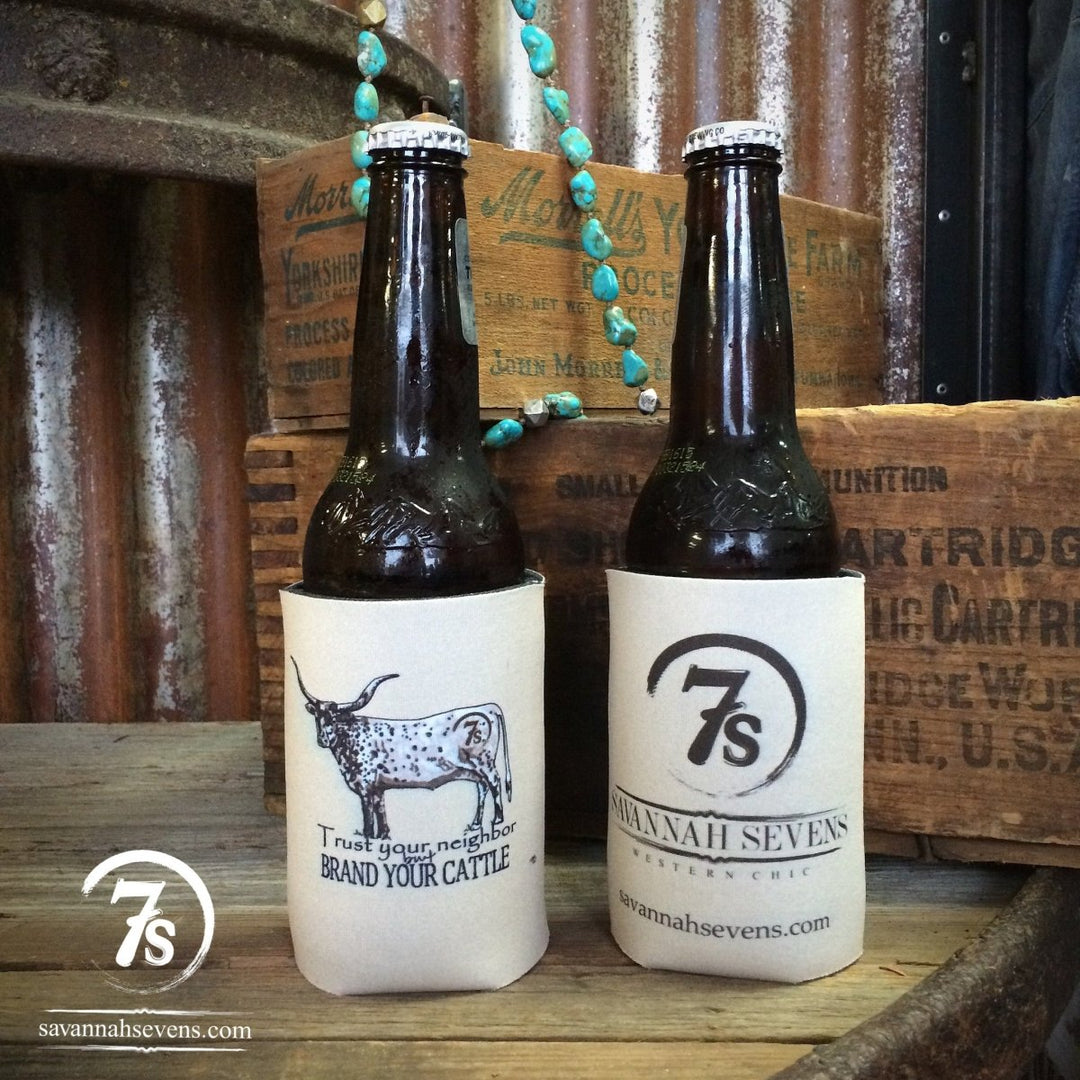 Two beer bottles in light bone Brand Your Cattle Koozies from Savannah Sevens western life{&}style sit on a wooden surface. One shows a longhorn and “Trust your neighbor... BRAND YOUR CATTLE,” the other has the 7s logo and savannahsevens.com—Western chic style.