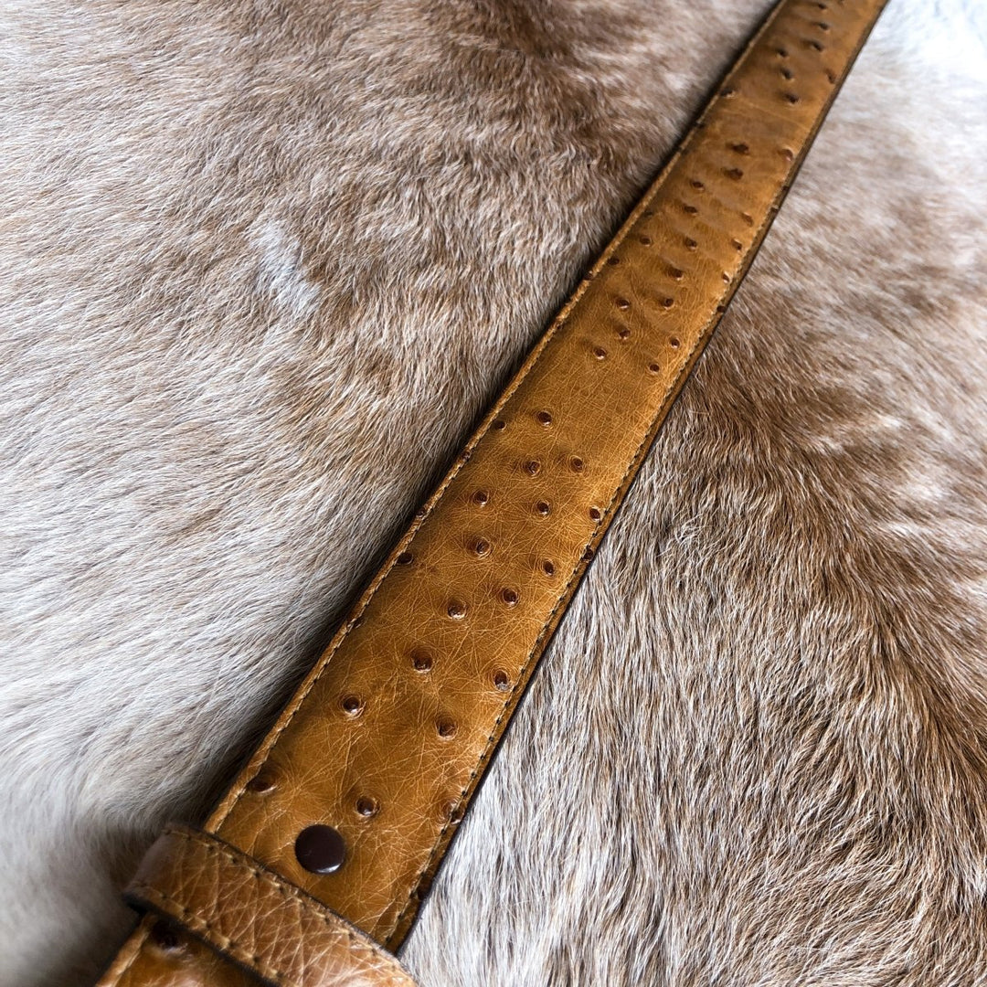 The Du Bois Belt by Savannah Sevens western life{&}style, made from handcrafted ostrich leather with a dotted texture, is displayed on light brown animal cowhide.