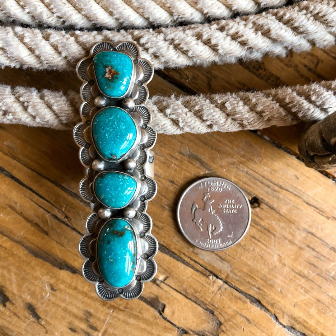 The Keomah Ring by Savannah Sevens western life{&}style, featuring four turquoise stones and a Southwest-inspired silver design, is displayed next to a Wyoming state quarter on wood with a coiled rope in the background.