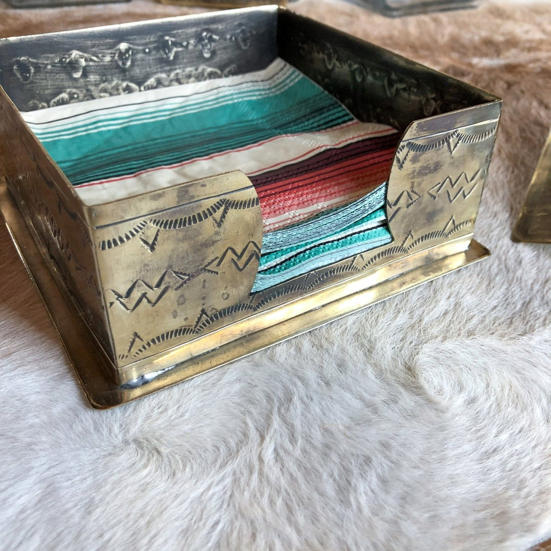 The La Puebla Cocktail Napkin Holder by Savannah Sevens western life{&}style, featuring engraved German silver and southwest accents, displays colorful napkins on a soft, light background.