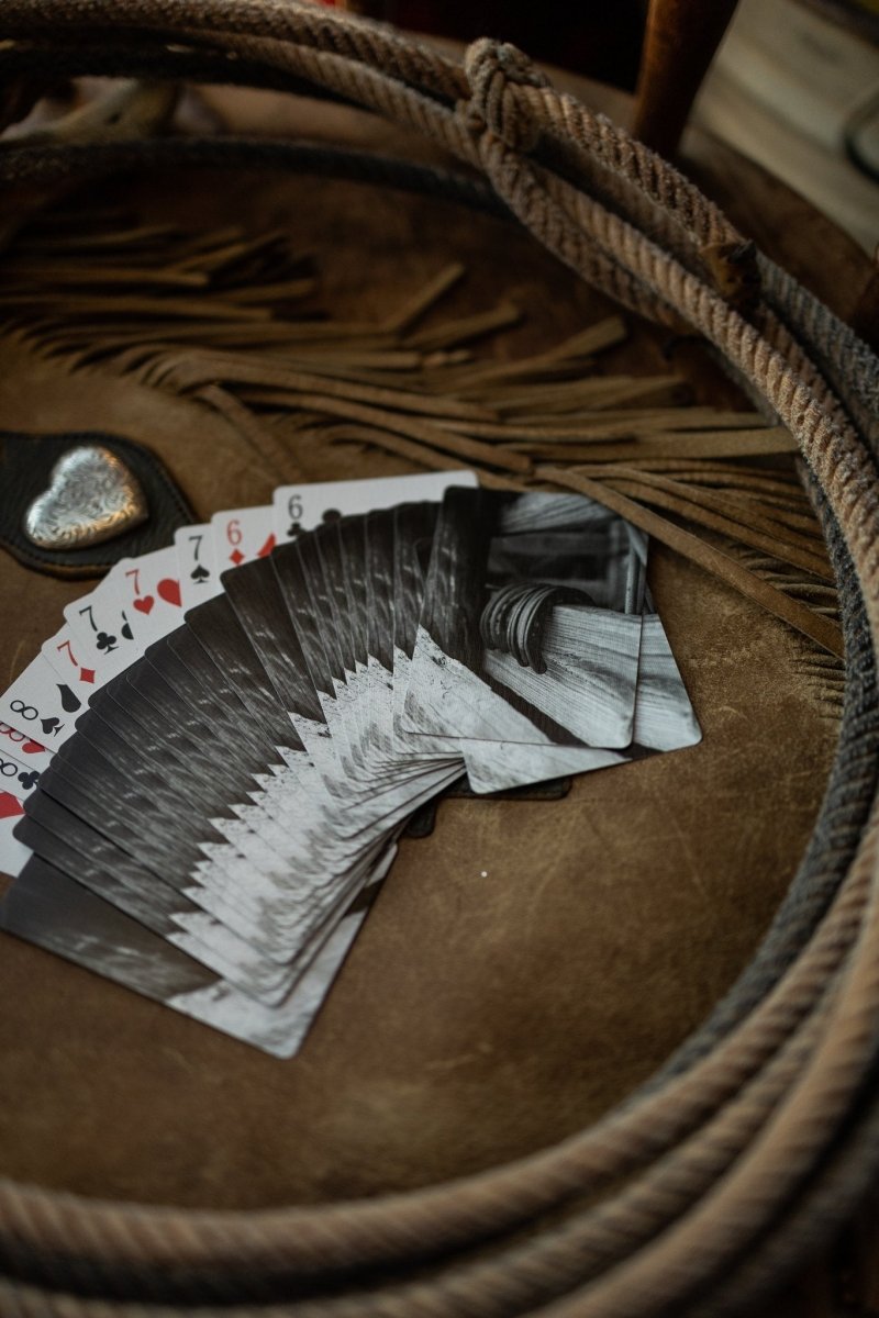 A fan of Lucky Playing Cards by Savannah Sevens western life{&}style lies face up on leather, surrounded by a coiled rope and silver heart, adding western charm to the scene.