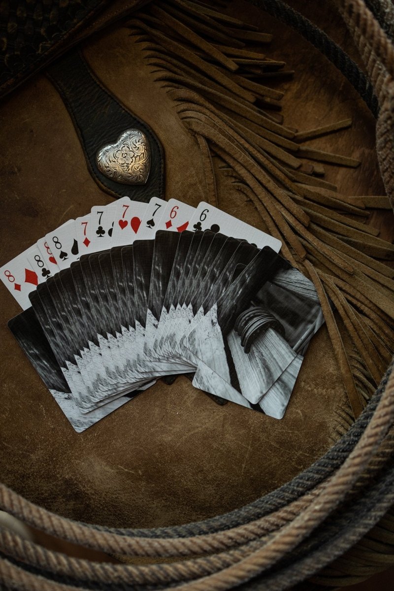 A fanned-out deck of Lucky Playing Cards by Savannah Sevens western life{&}style, showing pairs of eights, sevens, and sixes, rests on brown leather beside a coiled rope, a decorative belt buckle, and a lucky horseshoe.