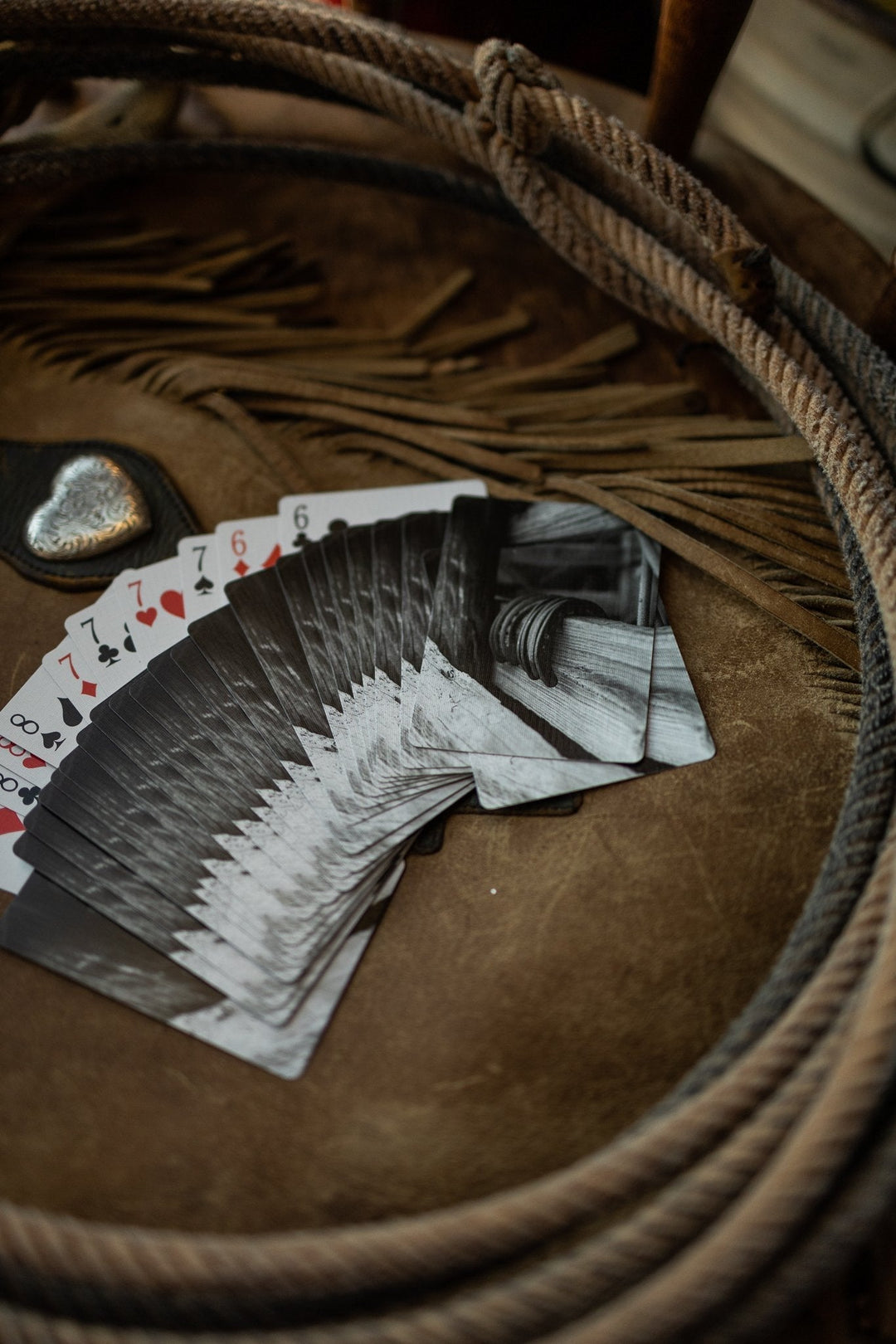 A fan of Lucky Playing Cards by Savannah Sevens western life{&}style lies face up on leather, surrounded by a coiled rope and silver heart, adding western charm to the scene.