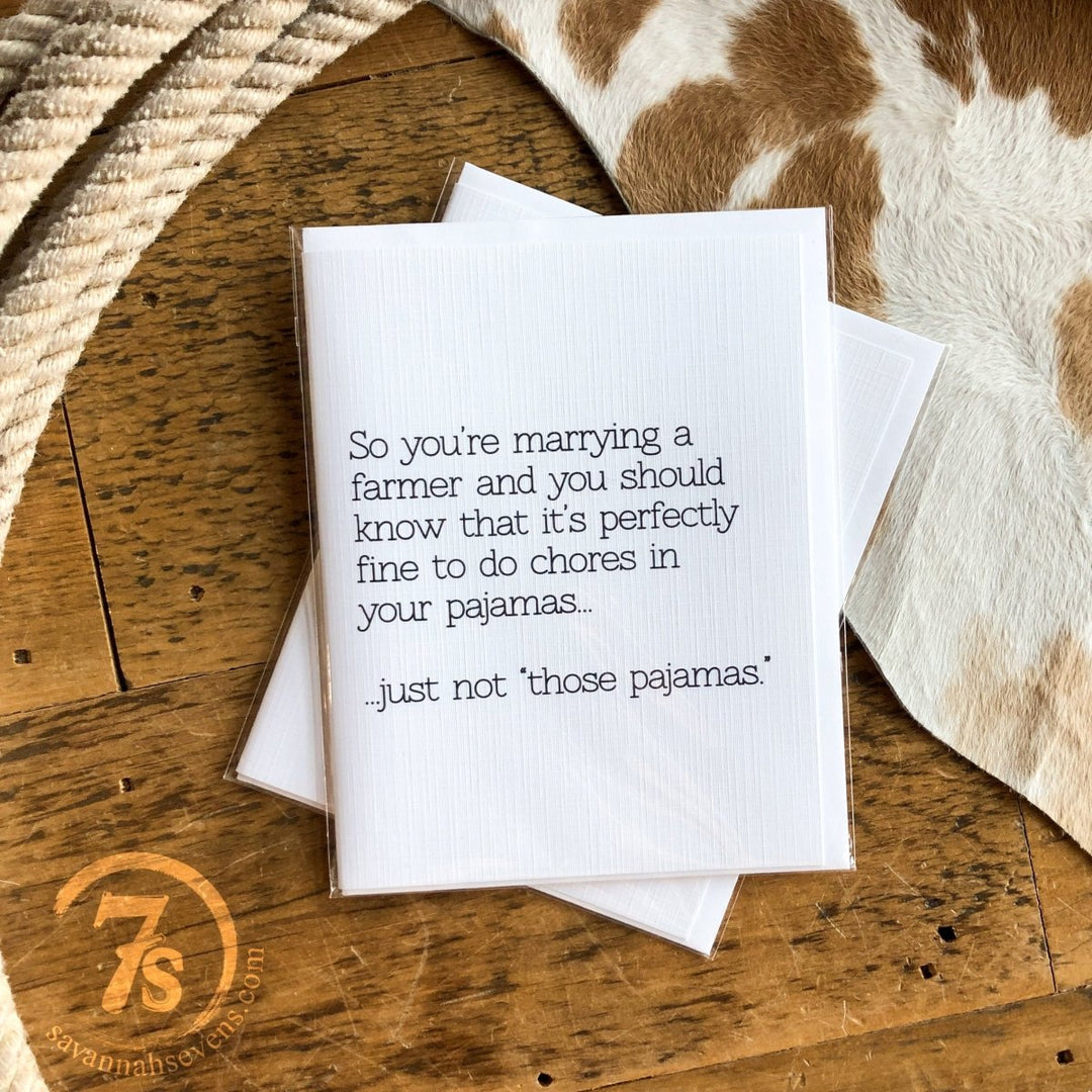 The Marrying A Farmer Card by Hungry Canyon sits on a wooden table, featuring the witty message: “So you’re marrying a farmer and it’s perfectly fine to do chores in your pajamas... just not those pajamas.” A cowhide rug is visible in the background.