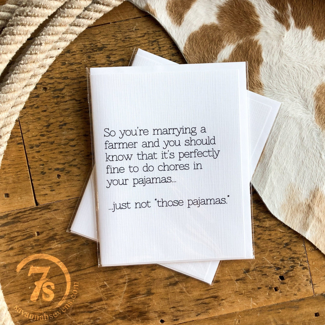 The Marrying A Farmer Card by Hungry Canyon sits on a wooden table, featuring the witty message: “So you’re marrying a farmer and it’s perfectly fine to do chores in your pajamas... just not those pajamas.” A cowhide rug is visible in the background.