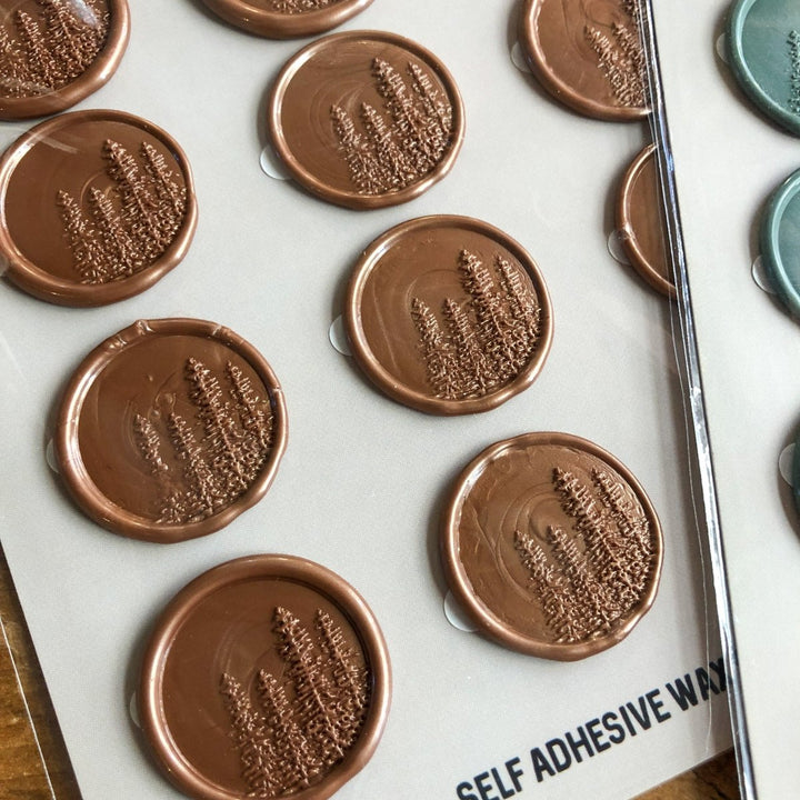 Pines Wax Seals by Savannah Sevens western life{&}style, featuring round bronze self-adhesive seals with embossed pine tree designs, are displayed in neat rows on a sheet with a sequoia green edge visible on the right.