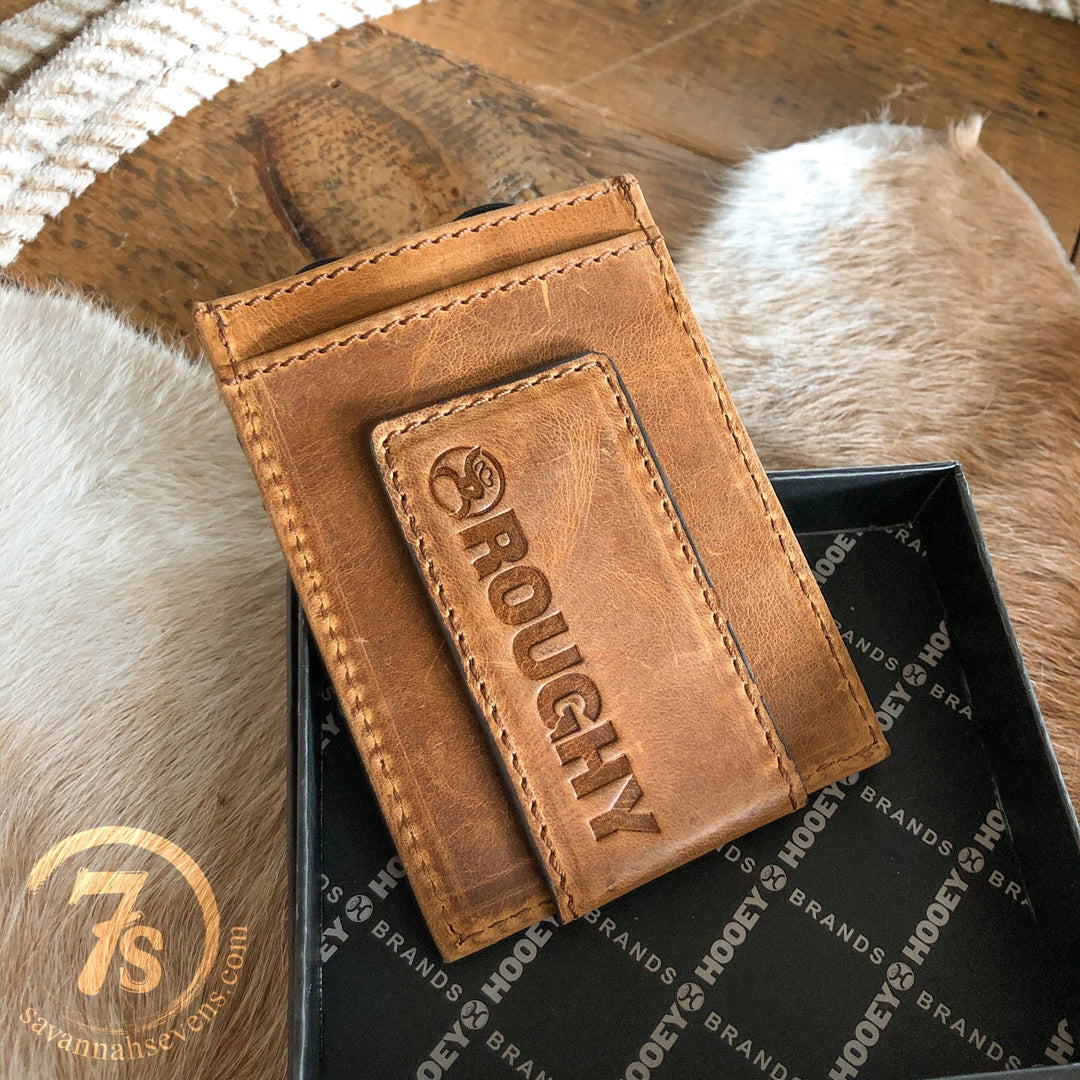 A Storden Money Clip wallet from Savannah Sevens western life{&}style, featuring brown distressed leather and ROUGHY embossed on the front, is shown in an open black box on animal fur with a round 7s logo close by.
