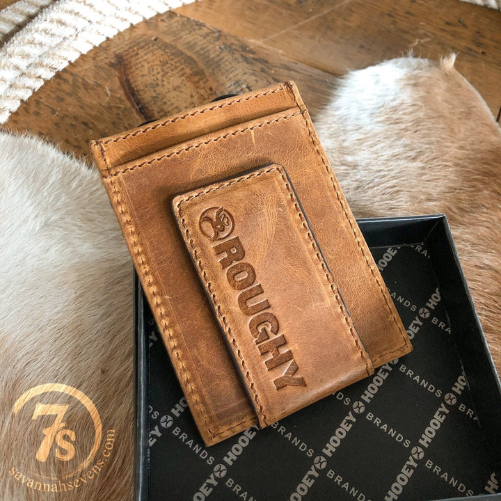 A Storden Money Clip wallet from Savannah Sevens western life{&}style, featuring brown distressed leather and ROUGHY embossed on the front, is shown in an open black box on animal fur with a round 7s logo close by.