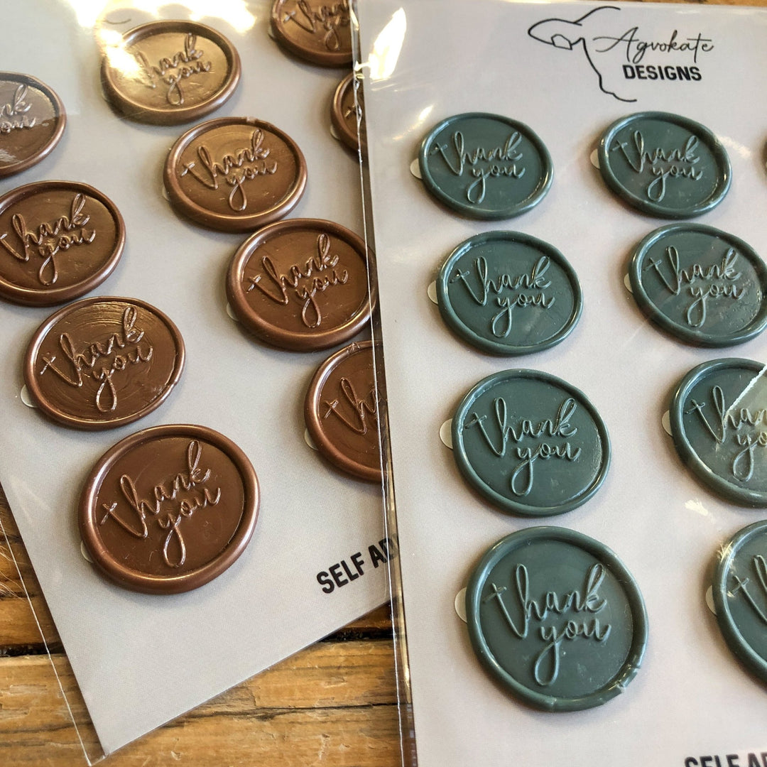 Two self-adhesive Thank You Wax Seal stickers by Savannah Sevens western life{&}style—one brown, one teal—each embossed with “thank you” in cursive, rest on a wooden surface.