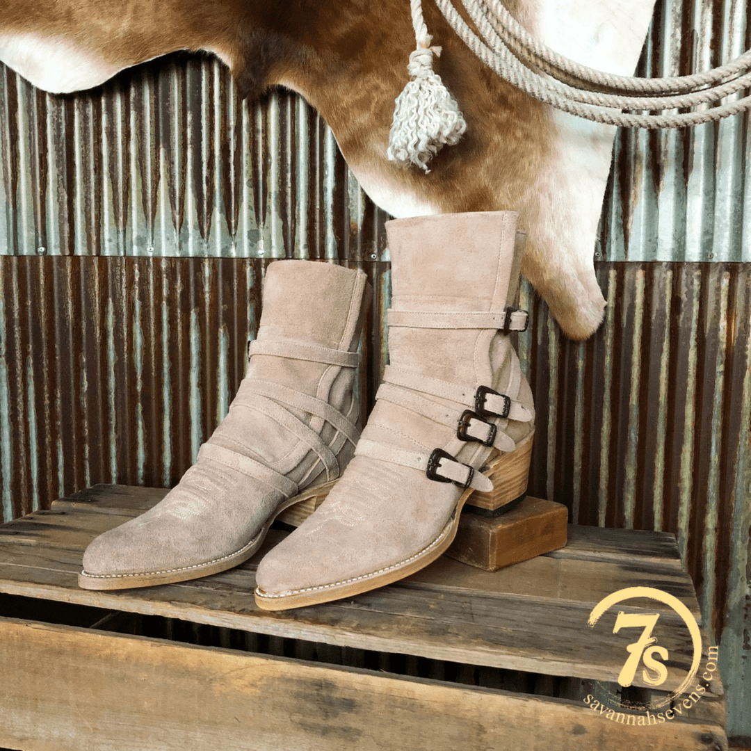The San Antone by Savannah Sevens western life{&}style: nude rough out leather booties with three side buckles and an almond toe, shown on a rustic crate. Cowhide and rope hang behind, with a “7S” logo in the lower right corner. Boots by Stetson.