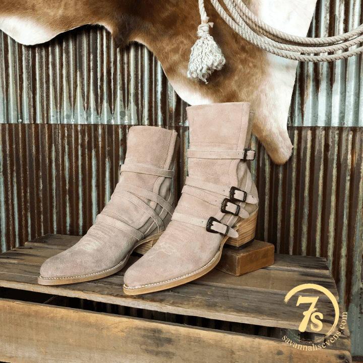 The San Antone by Savannah Sevens western life{&}style: nude rough out leather booties with three side buckles and an almond toe, shown on a rustic crate. Cowhide and rope hang behind, with a “7S” logo in the lower right corner. Boots by Stetson.