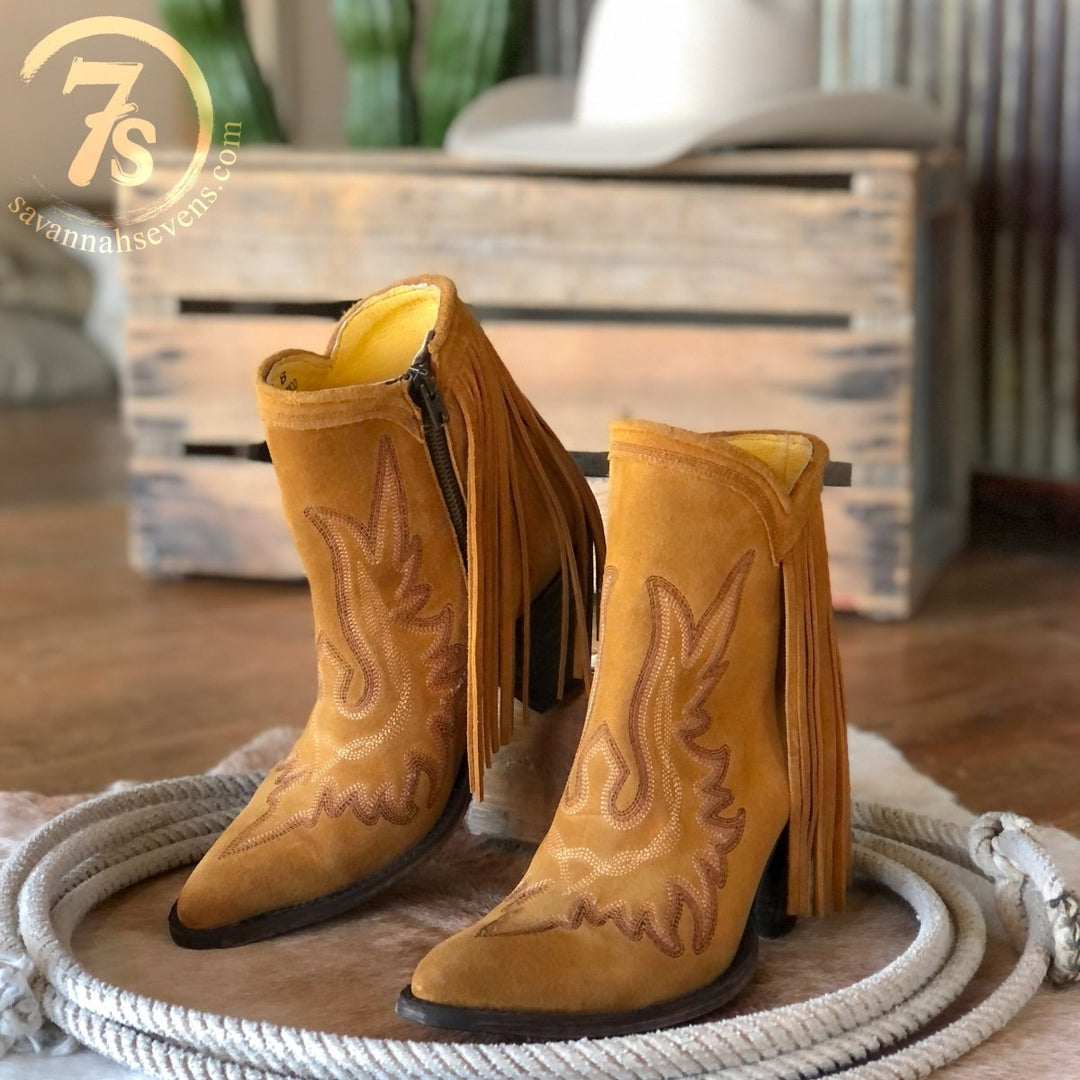 The Tejas tan suede western boots by Savannah Sevens western life{&}style, featuring decorative stitching and leather fringe, are shown on a coiled rope with a wooden crate and white cowboy hat. savannasevens.com logo in top left.