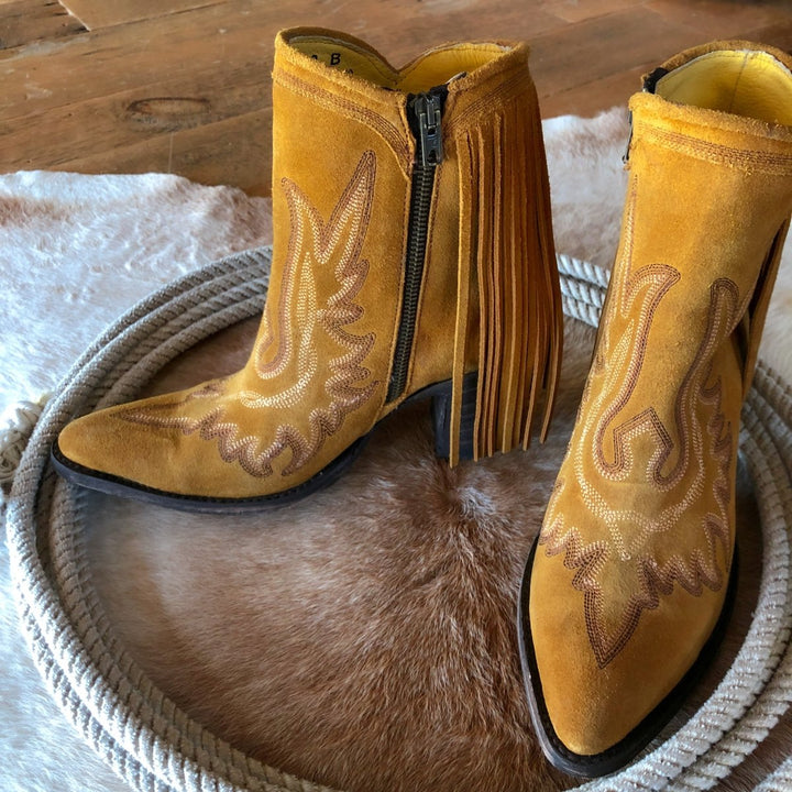 The Tejas yellow suede western boots with fringe and stitched designs by Savannah Sevens western life{&}style rest on a cowhide rug over a wooden floor, bringing classic style to the scene.